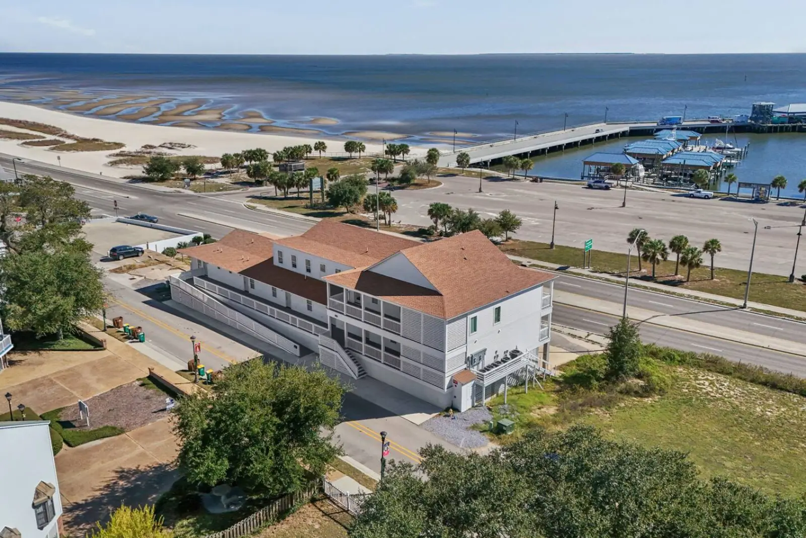 Aerial photo of a Nest Collection beachfront rental beside Pass Christian Harbor, with the sandy Gulf beach and pier just across the road.